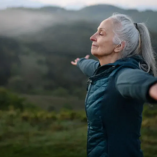 woman on a mountain top with her arms out taking a deep breath. high altitude breathing can be challenging but there are things that make it easier.